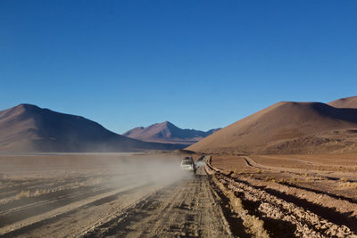 Car moving on landscape against clear blue sky