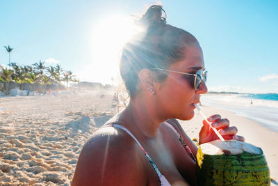 Close-up of woman drinking coconut water at beach during sunny day