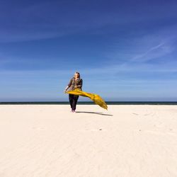 Cheerful woman holding scarf while walking on plaza bialogora beach