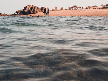 People on rocks at beach against sky