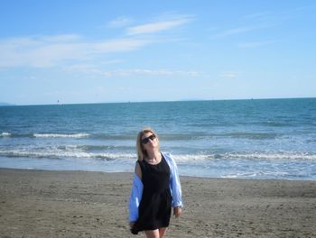 Rear view of woman standing at beach against sky