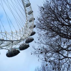 Low angle view of millennium wheel by bare tree against sky in city