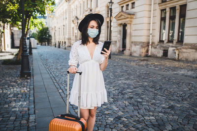 Woman wearing mask using smart phone standing on road