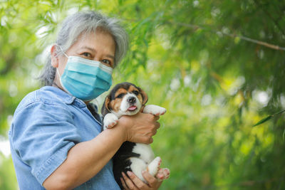 Portrait of woman wearing mask holding dog standing outdoors