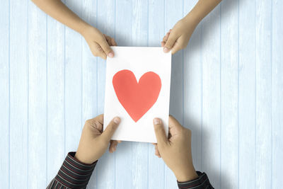 Cropped image of couple holding paper with heart shape on table