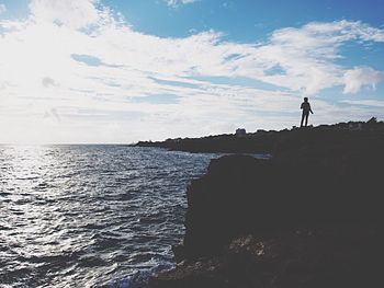 Silhouette man standing on rock by sea against sky
