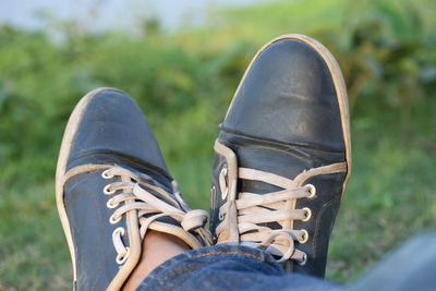 Low section of person wearing canvas shoes while sitting on grassy field