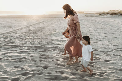 Side view of mother walking toddler twins to ocean with sun setting