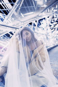 Portrait of young woman wearing scarf sitting against lights