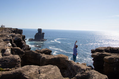 Man standing on rock by sea against sky