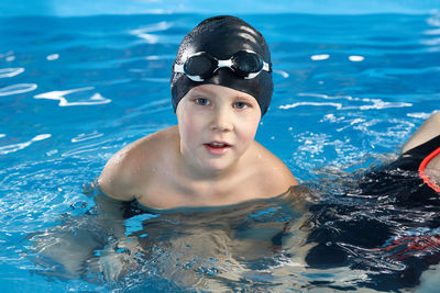 Preschool boy learning how to swim in a pool wearing swimming cap and goggles