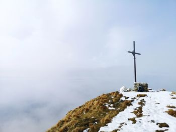 Cross on snowcapped mountain against sky