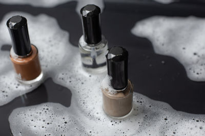 Three bottles of nail polish sit on a wet black floor. and with small soap bubbles follow 