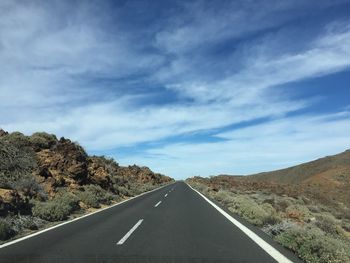 Empty road amidst mountain against cloudy sky