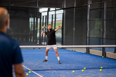 Monitor teaching padel class to man, his student - trainer teaches boy how to play paddle 