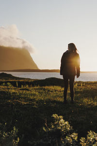 Rear view of silhouette woman standing at beach against sky during sunset