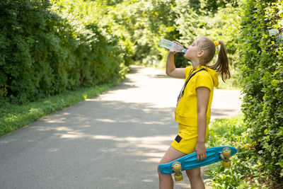 Side view of girl drinking water standing on road