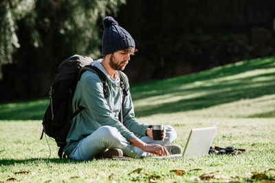 Man using laptop while sitting with coffee cup on grass