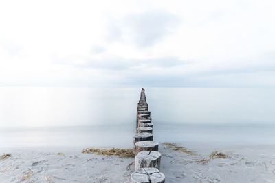 Wooden posts at beach leading towards sea against sky