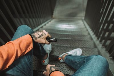 Low section of man holding electronic cigarette while sitting on steps