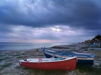 Boat moored on beach against dramatic sky