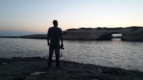 Rear view of silhouette man standing in sea against sunset sky