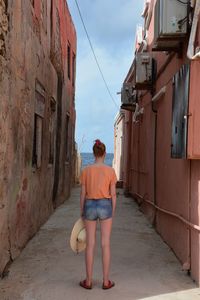 Full length rear view of woman standing amidst building against sky