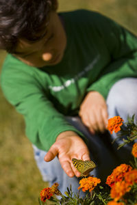 Boy looking at butterfly pollinating on orange flowers