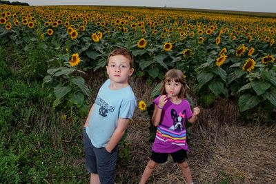 Siblings standing on flower field against clear sky during sunset