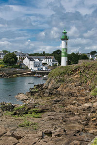 Lighthouse amidst sea and buildings against sky