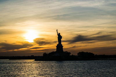 Silhouette statue of liberty against cloudy sky during sunset