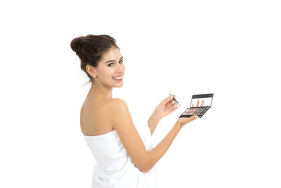 Portrait of young woman holding beauty product against white background