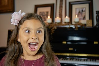 Close-up of surprised girl standing by grand piano