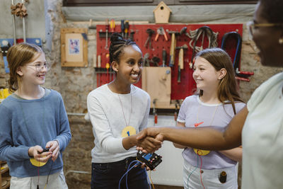 Smiling female student doing handshake with teacher during technology workshop at school