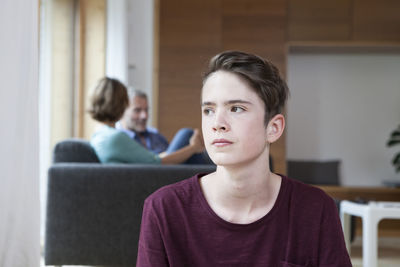 Thoughtful teenage boy at home with parents in background