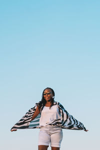 Portrait of young woman standing against clear sky