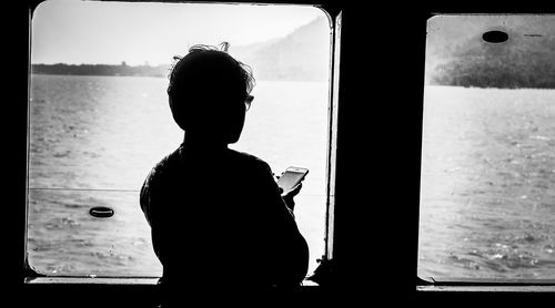 Rear view of silhouette man sitting by window