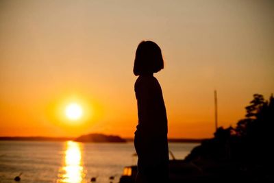 Silhouette woman looking at sea against sky during sunset