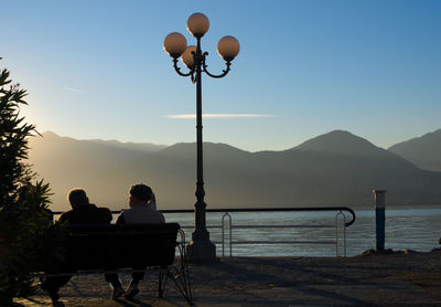People sitting on bench at pier against sky
