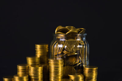 Close-up of coins in jar against black background