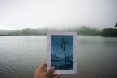 Person photographing lake against sky