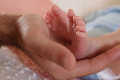 Cropped hand of father holding newborn baby feet at home
