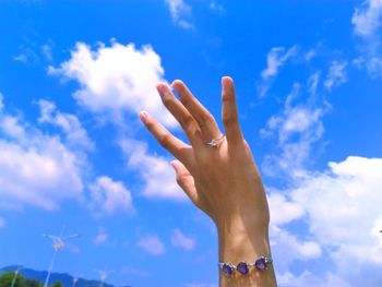 Low angle view of woman wearing ring and bracelet against blue sky