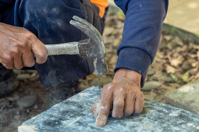 Midsection of man hammering nail on plank