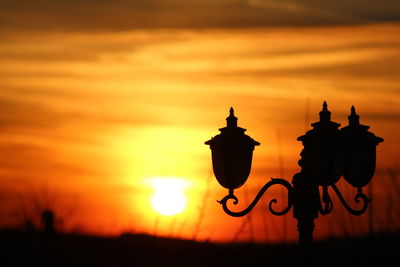 Silhouette lamp on field against orange sky