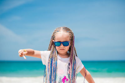 Girl wearing sunglasses while gesturing at beach against sky