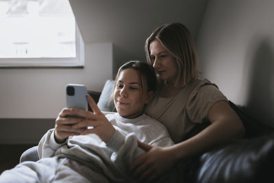 Homosexual couple sitting on sofa and using cell phone