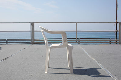 Empty chair by sea against sky