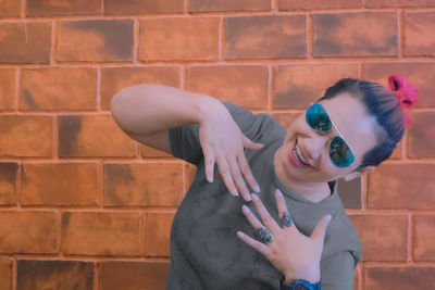 Portrait of smiling young woman standing against brick wall