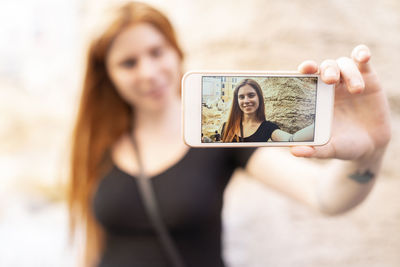 Positive young female taking selfie with smartphone in city